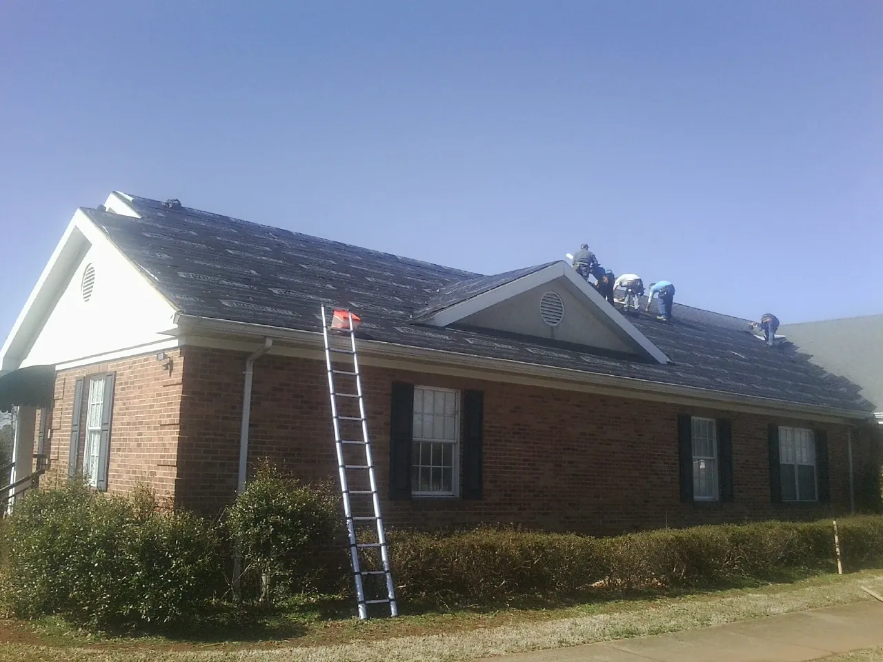 Crew tearing shingles off a brick ranch roof with a ladder set — Emergency Roof Repair work by our crew in Bridgton