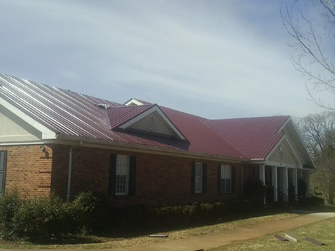 Red metal roof with gabled entries on a long brick building, from a Hail Damage Roof Repair job in Bridgton