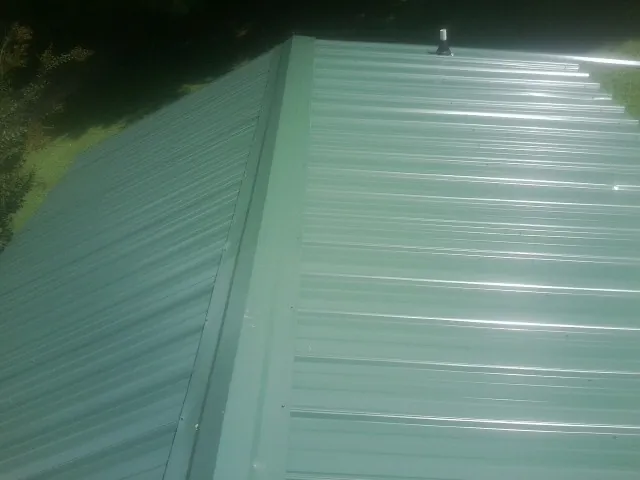 New green metal panels meeting at the ridge of a roof — Flat Roof Repair work by our crew in Bridgton