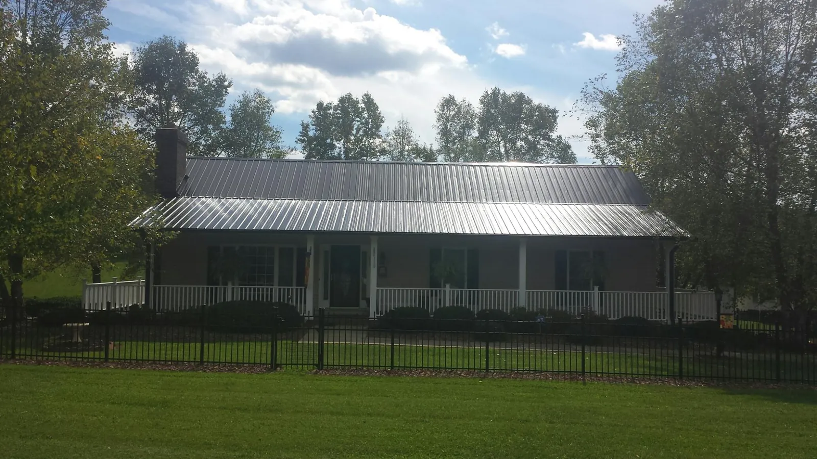 Gray metal roof on a brick ranch with a full width front porch — Gutter Guard Installation work by our crew in Bridgton