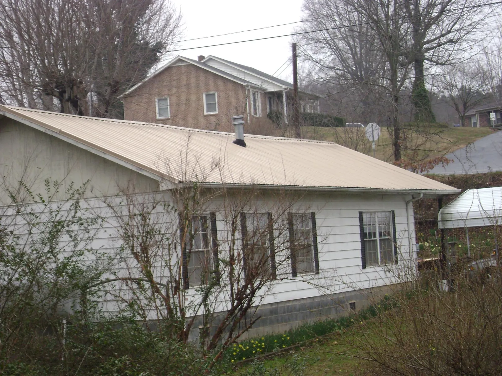 Tan metal roof on a white sided house set into a hillside — Commercial Roofing by Roofing Brothers in Bridgton