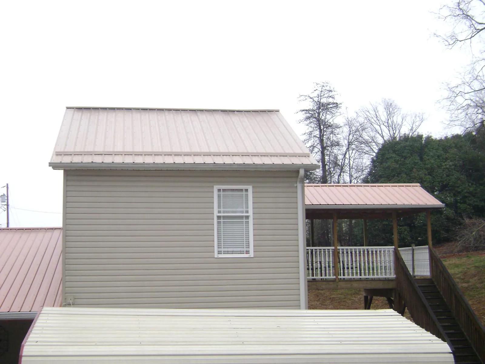 Tan metal roofs on a two story addition and attached porch, from a Roof Replacement job in Bridgton